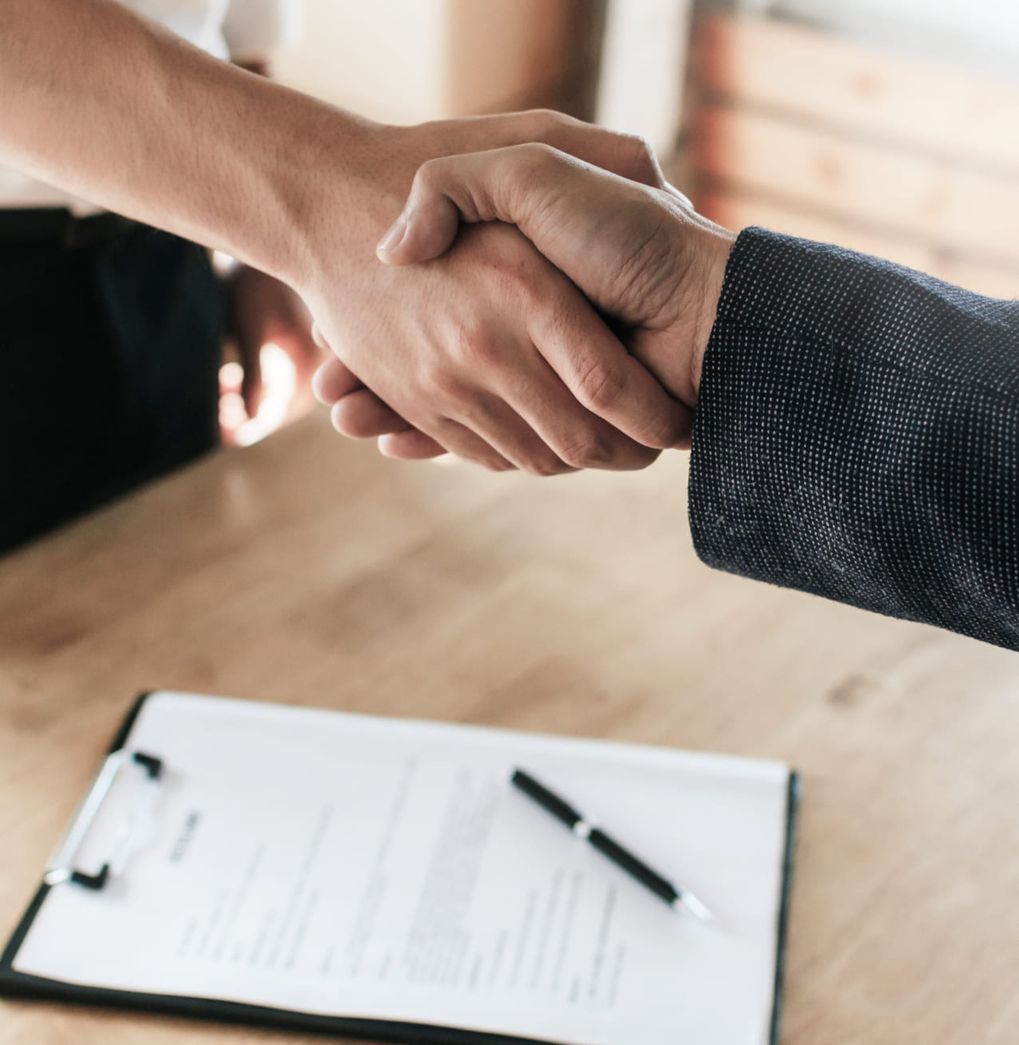 Zwei Personen schütteln sich über eine Klemmbrett die Hände